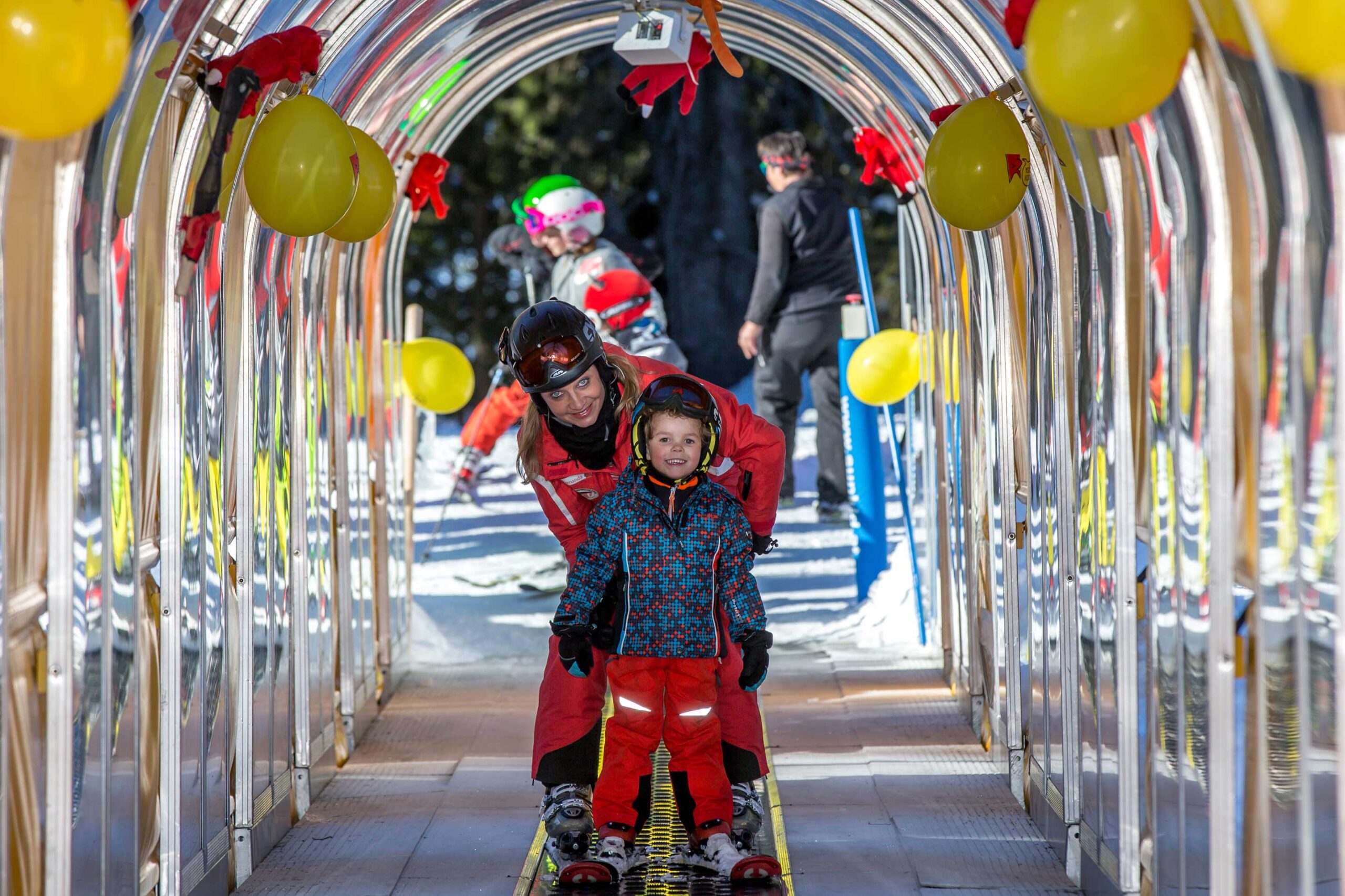Ein Kind ist mit seinem Skilehrer auf dem Zauberteppich mit Musikbox im Skigebiet Grüsch Danusa